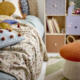 Filipa Floral Cotton Throw in multi draped over a bed, showing the all-over fern and floral print alongside cushions and a child's bedroom shelving unit.