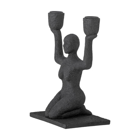 Lucie Resin Candle Holder in black, a textured kneeling female figure raising both arms to hold two cup-shaped candle sockets, on a rectangular base against a white background.