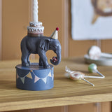 Multicoloured 18cm resin elephant candle holder in a party hat, carrying a tiered cake on a bunting-decorated base with a lit white candle, on a wooden shelf.