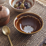 Heikki Floral stoneware bowl in brown with a white flower motif and wavy rim line, shown with a bowl of olives, gold spoon, and wooden grinder.