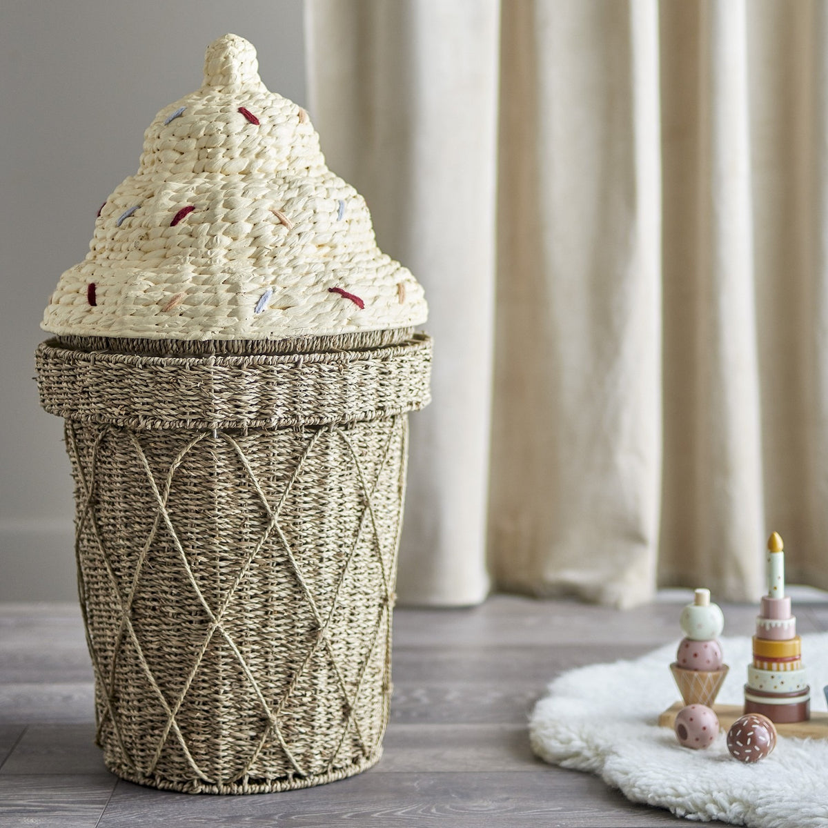 Cillie Seagrass Basket with Lid 72cm, ice-cream cone-shaped kids storage basket with criss-cross woven base and swirled sprinkle-dotted lid, shown in a nursery setting beside toys.