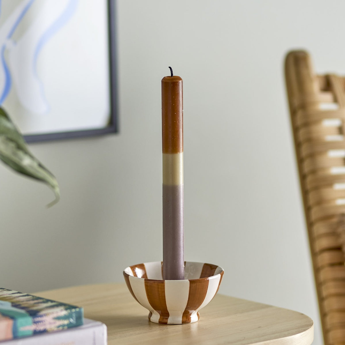 Dip Dye Fluted Candle in brown, cream, and mauve bands, displayed in a striped ceramic candle holder on a wooden side table in a living room setting.