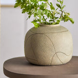 Niza Terracotta Vase 16.5cm in natural, a round, textured vase with a narrow raised-rim neck and etched curved line pattern, shown holding green foliage on a dark side table.