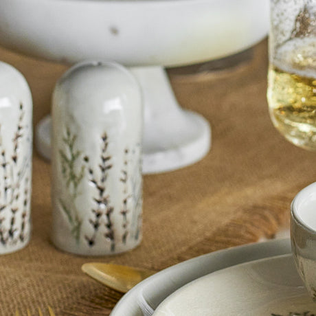 Bea Stoneware Salt & Pepper Shakers in cream, tall domed ceramic bodies with floral sprig detail, shown on a dining table beside glassware and a cake stand.