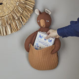 Toto Linen Wall Basket in brown, a kangaroo-shaped fabric storage holder with quilted front pouch, shown mounted on a wall holding a book as a hand reaches inside.