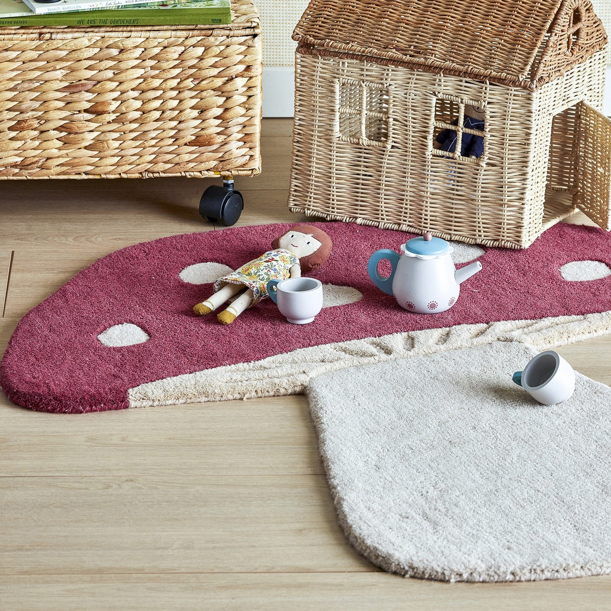 Mushroom Wool Rug 90x85cm in red, shaped like a toadstool with white spots and stalk, shown on a wooden floor with a doll and toy teapot set.