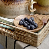 Tiara wooden acacia bowl from the set of 2 shown filled with blueberries on a woven basket tray, styled with mugs and books in a kitchen setting.