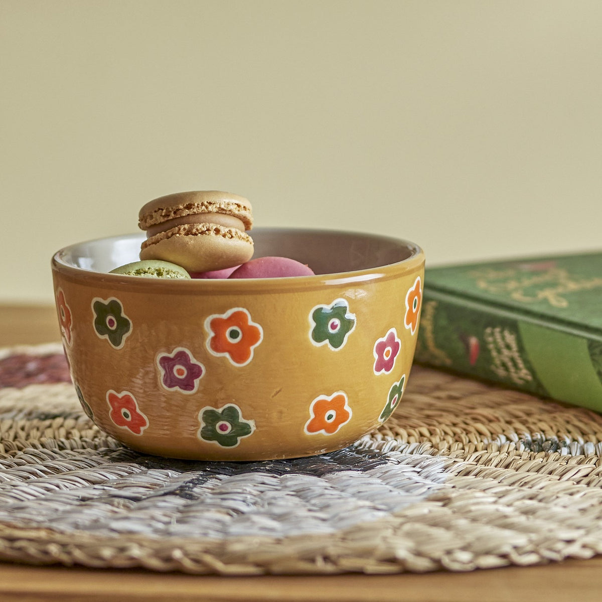 Addy Stoneware Bowl 12cm in brown with multicoloured flower pattern, filled with macarons and sweets on a woven placemat beside a book.