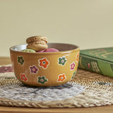 Addy Stoneware Bowl 12cm in brown with multicoloured flower pattern, filled with macarons and sweets on a woven placemat beside a book.