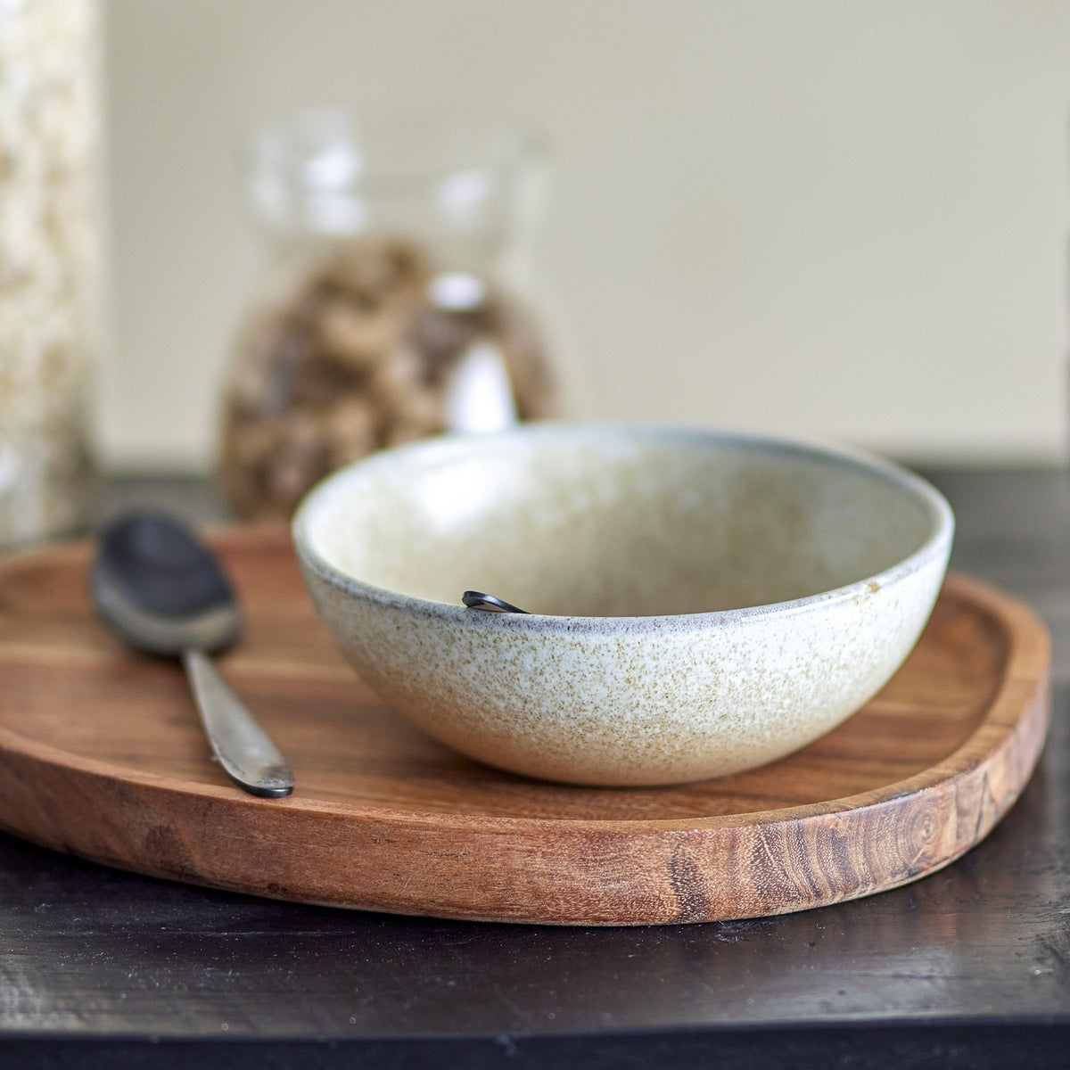 Paula Stoneware breakfast set bowl in beige reactive glaze on a wooden tray, shown with a dark spoon and blurred jar in a kitchen setting.