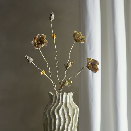 Poppy Artificial Stem in brown fabric, with wavy branching stems holding open flower heads and closed buds, displayed in a ridged vase against a muted neutral room setting.