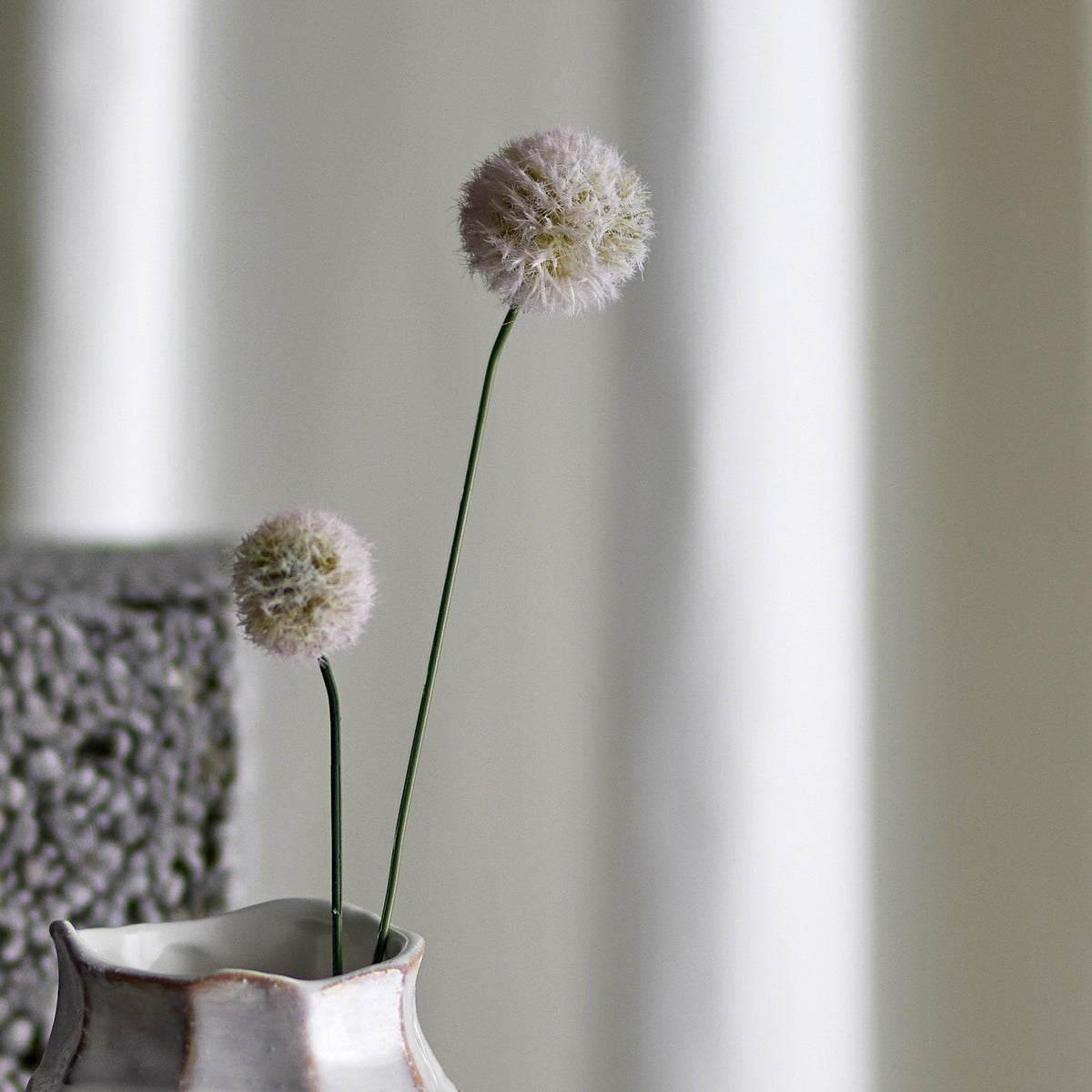 Phlox Artificial Stem in cream, showing two fluffy round flower heads on slender green stems in a textured ceramic vase against a softly blurred neutral backdrop.
