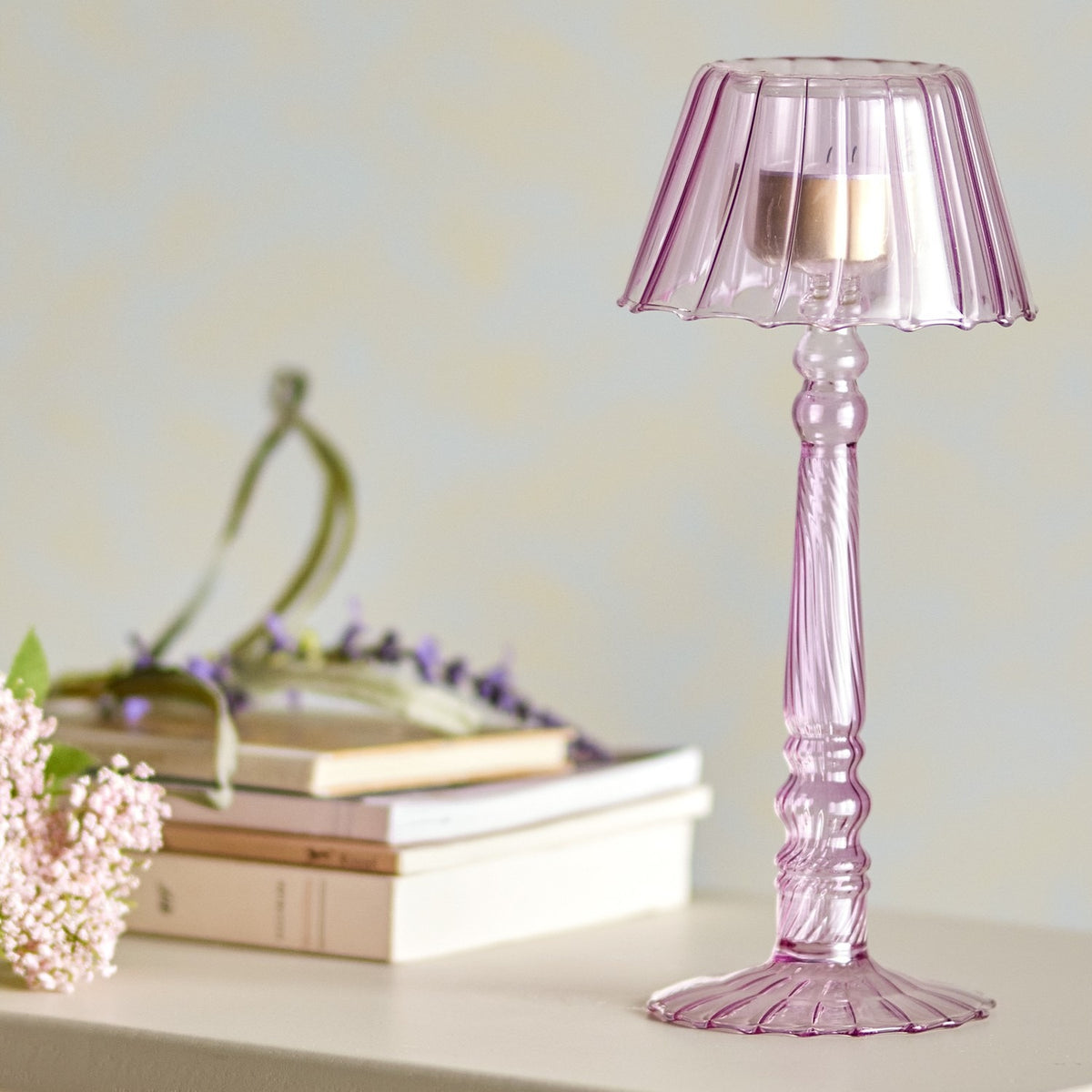 Cisco Glass Tealight Holder 23.5cm in pink, lamp-shaped with fluted scalloped shade and ribbed spiral stem, shown on a shelf beside books and flowers.