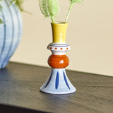 Kairi Stoneware Vase 14cm in Multi, shown with a flared yellow neck, dotted white collar, orange rounded mid-section and blue flared foot, holding greenery on a dark surface.