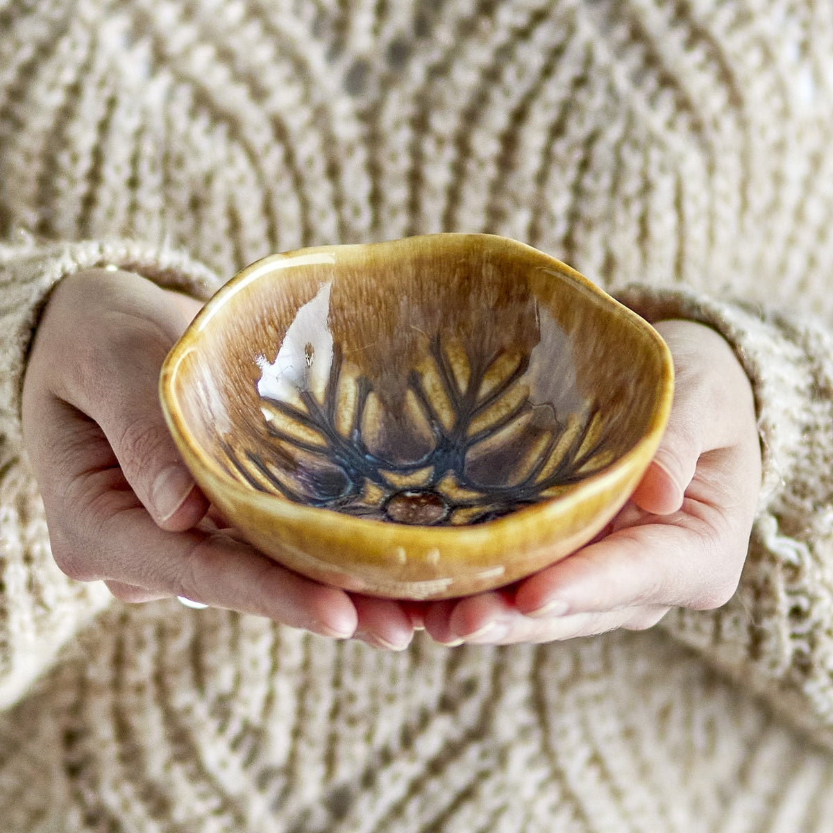 Hands holding the Acco Stoneware Christmas Bowl 12cm in brown, a small wavy-rimmed ceramic bowl with a radiating frost-like glaze pattern inside.