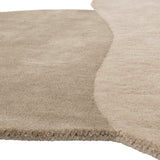 Close-up of the Denton Wool Rug 140x110cm in brown, showing overlapping pebble-like shapes in light and deeper brown tones with a soft wool pile and curved edge.