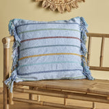 Frey Striped Cotton Cushion in blue with multicoloured horizontal stripes and fringed edges, shown on a bamboo bench in a room setting.