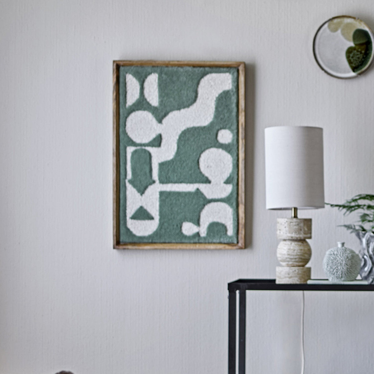 Longton Wool Wall Decor in green, a tufted abstract wall art piece in a slim wood frame, shown above a console table with a lamp in a living room setting.