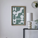 Longton Wool Wall Decor in green, a tufted abstract wall art piece in a slim wood frame, shown above a console table with a lamp in a living room setting.