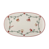 Yule Oval Stoneware Christmas Platter in cream, featuring a pine sprig garland with hearts, drum, pig, horn, candy cane and pretzel motifs, edged in red, on a white background.