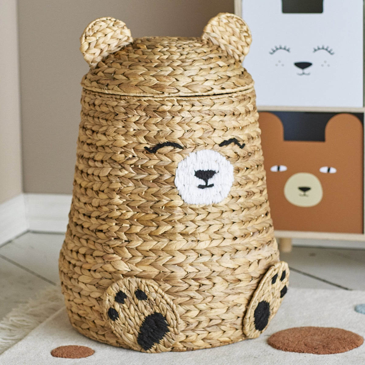 Timone Bear Water Hyacinth Basket with Lid in natural woven finish, featuring ear-shaped lid, stitched smiling face and paw details, shown in a nursery setting.