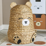 Timone Bear Water Hyacinth Basket with Lid in natural woven finish, featuring ear-shaped lid, stitched smiling face and paw details, shown in a nursery setting.