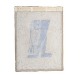 Atle Wool Wall Decor in multi, a woven wool tapestry with a blue figural motif bordered by a leafy sprig pattern, hung from a wooden rod on a white background.