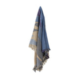 Maji Cotton Throw in Multi hangs against a plain white background, showing abstract overlapping blocks in blue, tan, and grey with a flecked, tweedy texture and raw fringed edges.