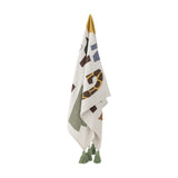 Memmo Cotton Throw in multicoloured cotton, hanging with bold abstract letter shapes in green, mustard, brown and blue, finished with green tassels, on a plain white background.