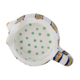 Overhead view into a cat-shaped stoneware candle holder's hollow bowl, white with green polka dots inside and gold-and-blue striped rim and handle, on a white background.