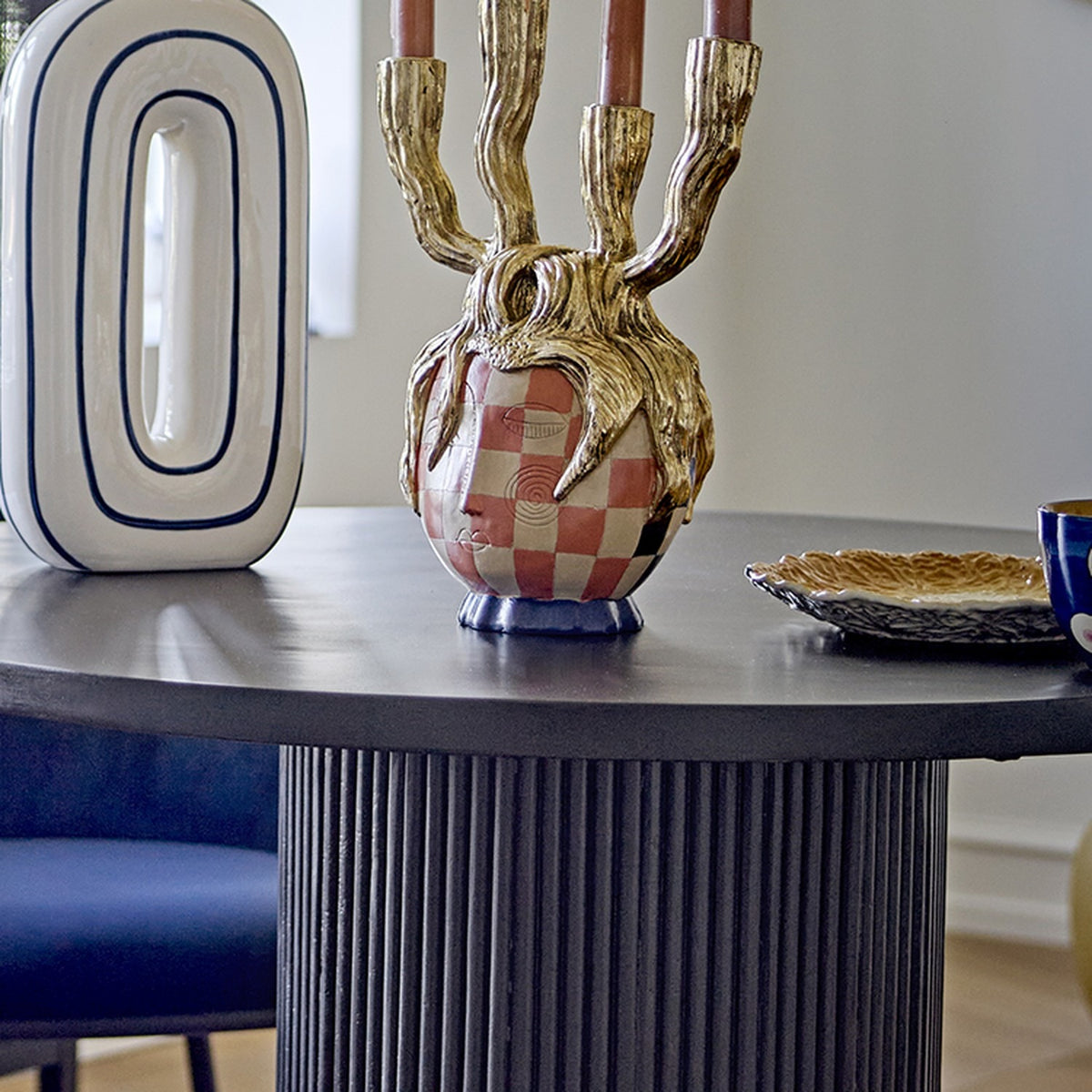 Medusa Resin Candle Holder in gold with four branching candelabra arms over a pink and white checked face design, shown on a dark round table with pink taper candles.