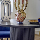Medusa Resin Candle Holder in gold with four branching candelabra arms over a pink and white checked face design, shown on a dark round table with pink taper candles.