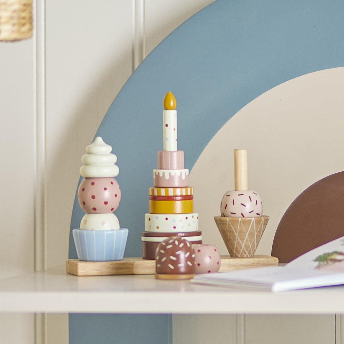 Celebrate 18-Piece Dotted Wooden Activity Toy in multi, three beech stacking towers—ice cream cone, tiered birthday cake with candle, and cupcake—on a wooden base, shown on a shelf.
