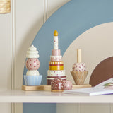 Celebrate 18-Piece Dotted Wooden Activity Toy in multi, three beech stacking towers—ice cream cone, tiered birthday cake with candle, and cupcake—on a wooden base, shown on a shelf.