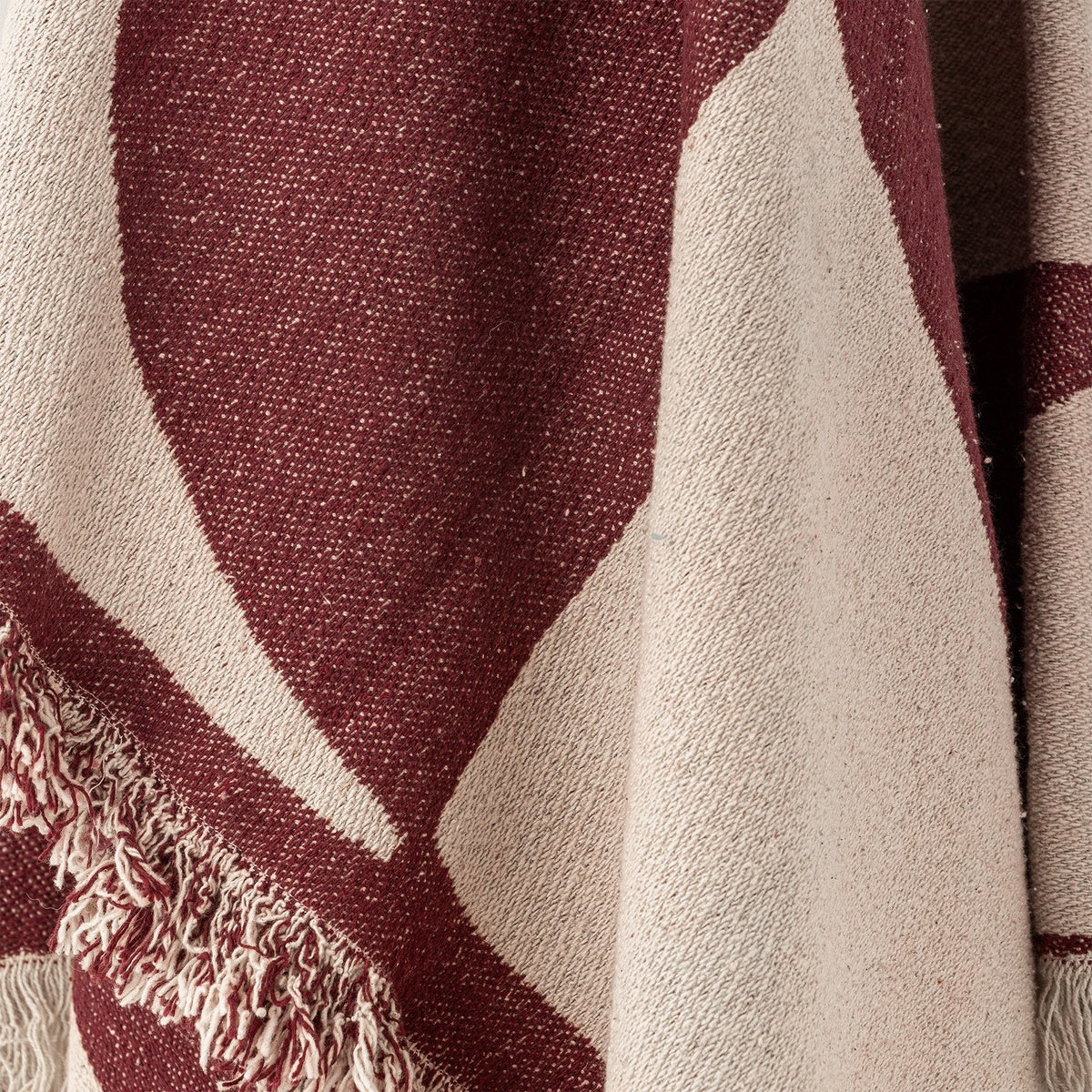 Close-up of the Olica Cotton Throw in red, showing woven texture with large curved cream shapes and a loose fringed edge.