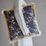 Eydis Floral Cushion in multicoloured fabric with dense floral print and fringe trim, shown held by a person in a neutral-toned setting.