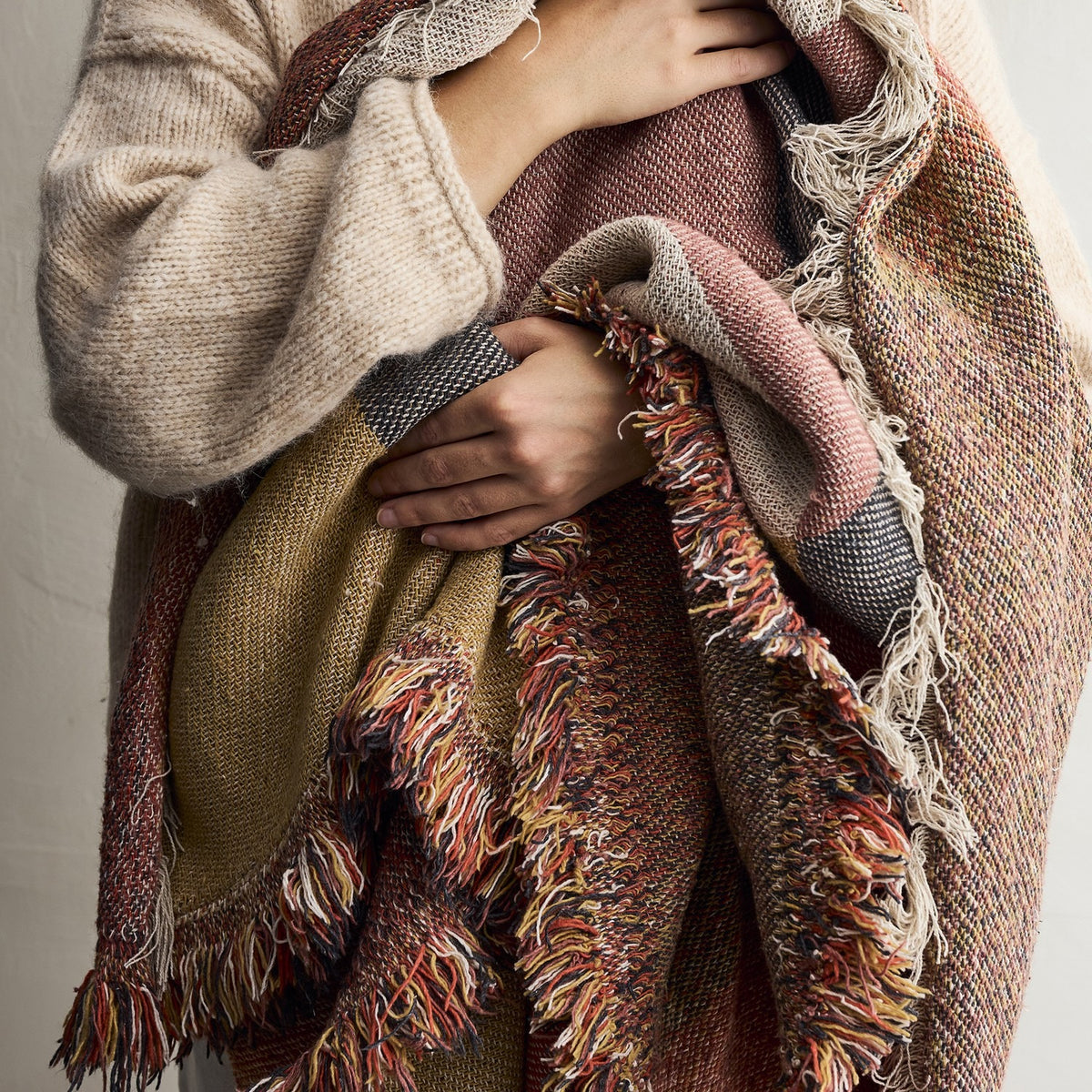 Arni Throw in Multi draped over the arm, showing the woven fabric with curved colour-block panels in rust, mustard and pink, finished with a long mixed-yarn fringe.