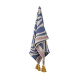 Arlie Throw in blue, a woven fabric throw with swirling bands and straight stripes, finished with mustard corner tassels, hanging against a plain white background.