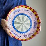 Missy Striped Stoneware Tray held in hand, round ceramic serving dish with blue cat motifs, scalloped blue centre ring, and red and yellow striped rim.