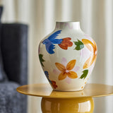 Maricala Floral Stoneware Vase 27cm in white with hand-painted birds, flowers and leaves in blue, orange and green, shown on a mustard side table in a living room.