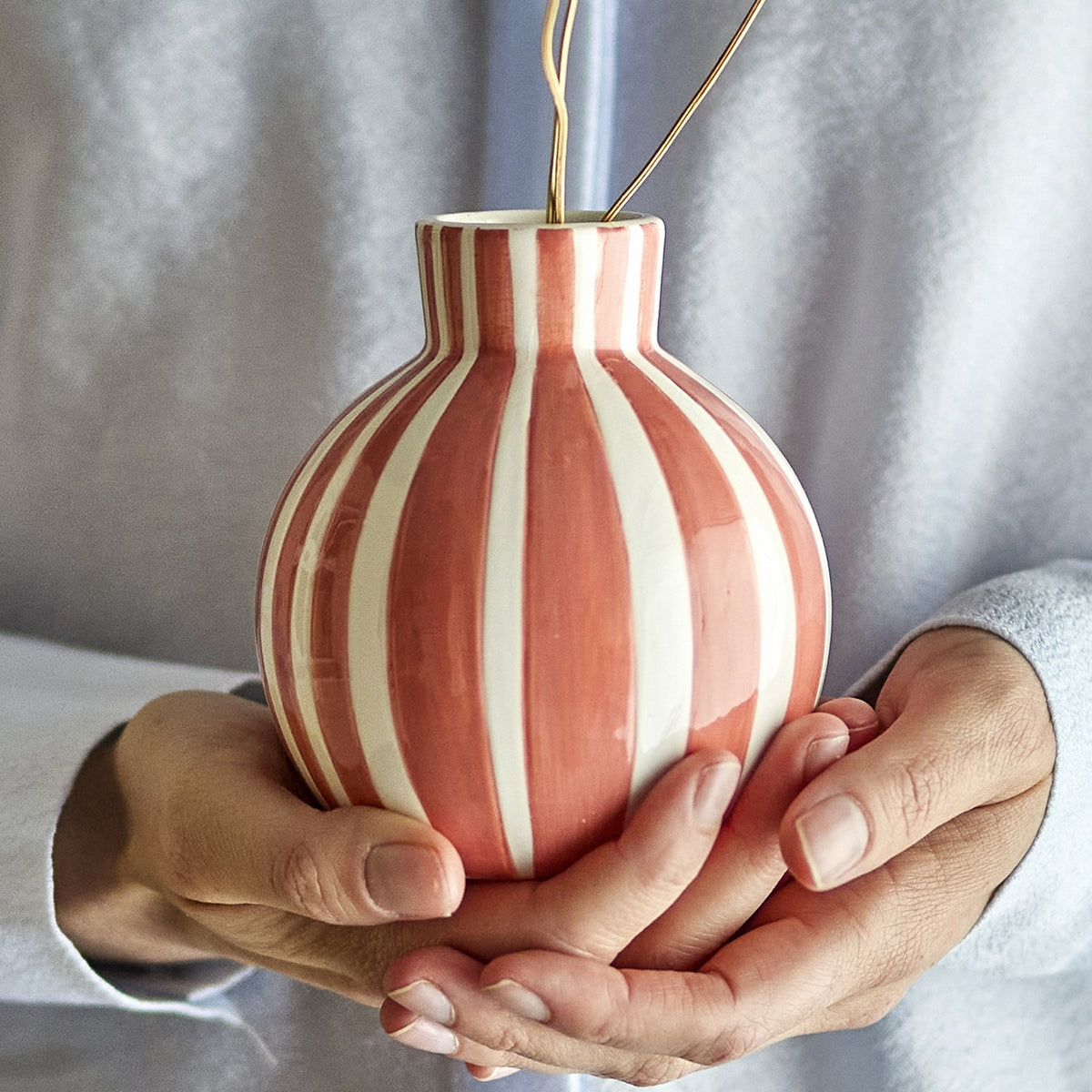 Fian Striped Ceramic Vase 11cm in orange and white, hand-painted round dolomite vase held in two hands, with gold stems inside.