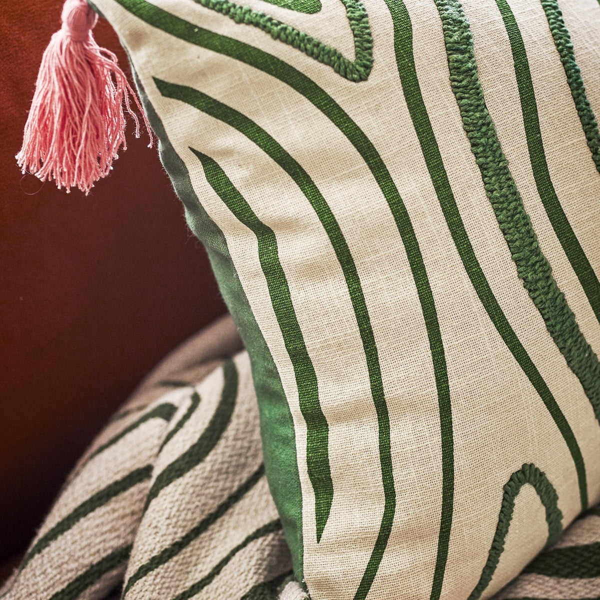Woodsby Cotton Cushion in Multi, close-up showing green woodgrain-style swirl pattern with printed and tufted lines on cream cotton, pink corner tassel visible.