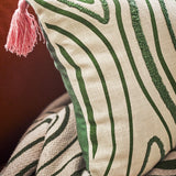 Woodsby Cotton Cushion in Multi, close-up showing green woodgrain-style swirl pattern with printed and tufted lines on cream cotton, pink corner tassel visible.