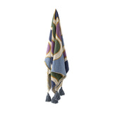 Salacia Throw in Multi hanging against a plain background, showing curved bands in blue, green, purple, and mustard with fringed tassel corners.