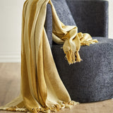 Frello Striped Cotton Throw in yellow with alternating deep and pale stripes and fringed edges, draped over a dark grey upholstered armchair.