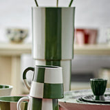 Floki Striped Stoneware Vase 31cm in Green, tall rounded ceramic form with hand-painted vertical stripes, shown on a table with mugs and bowls in a living room setting.