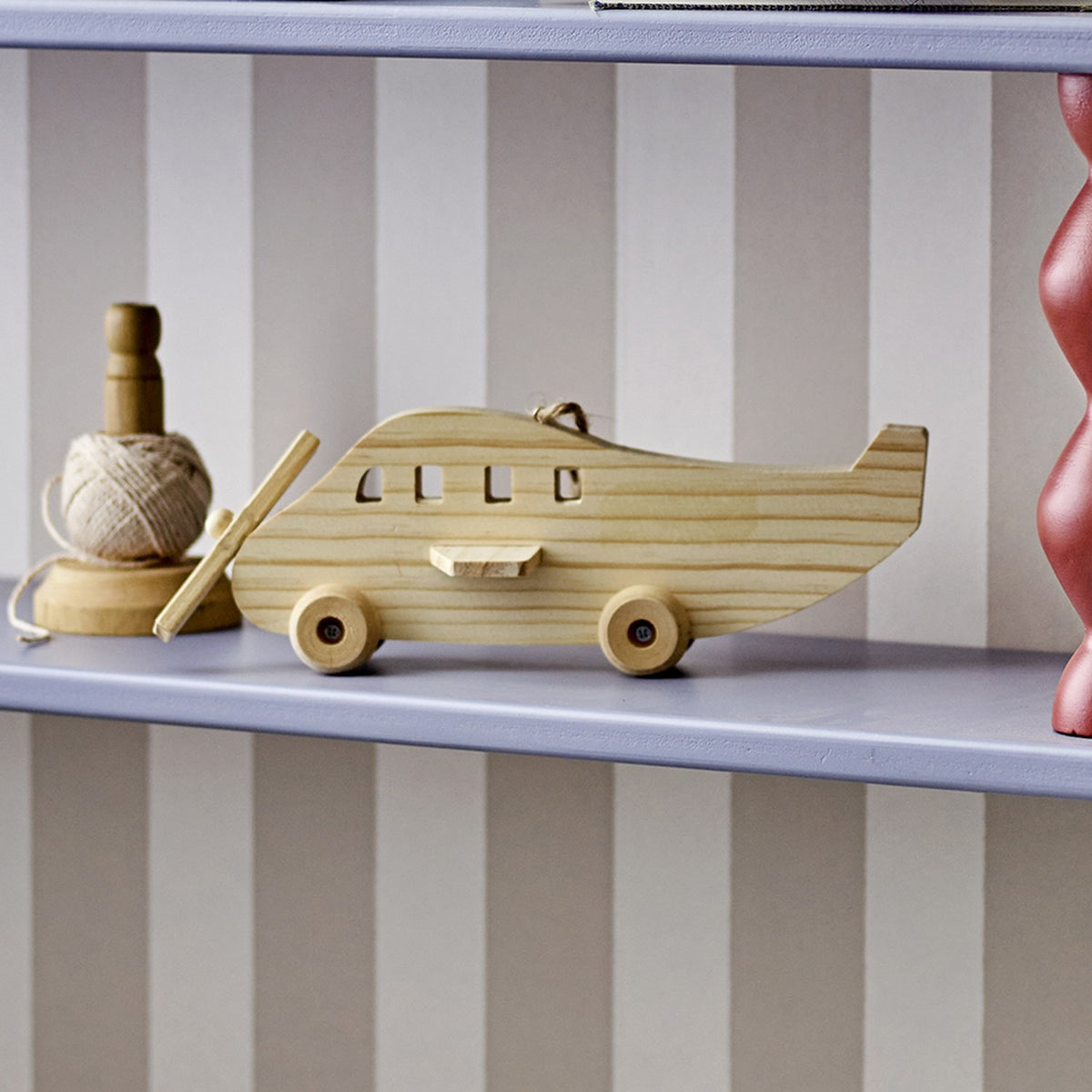 Plane Wooden Baby Mobile in natural pine with window cut-outs, wings, propeller and wheels, displayed on a light grey shelf beside a ball of twine.