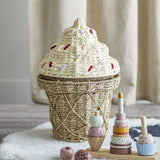 Cillie Seagrass Basket with Lid 41cm in Natural, shaped like an ice cream cone with a criss-cross woven base and a stepped swirl lid dotted with coloured sprinkle stitches, shown with toy figures.