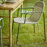 Calana Iron Garden Chair in grey, with a powder-coated metal frame and woven basketweave seat and curved back, shown outdoors beside a wooden table on grass.