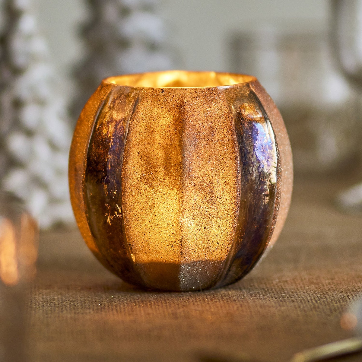 Felecia Striped Glass Christmas Tealight Holder in gold, round 10cm glass votive with alternating grainy and smooth iridescent vertical stripes, lit and shown on a textured tablecloth.
